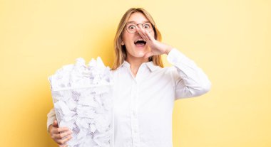 Güzel sarışın kız kendini mutlu hissediyor, elleri ağzının kenarında bağırıyor. kağıt toplar çöp konsepti