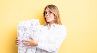 Güzel sarışın kız omuz silkiyor, kafası karışık ve kararsız. kağıt toplar çöp konsepti