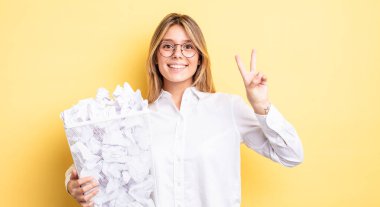 Güzel sarışın kız gülümsüyor ve arkadaş canlısı görünüyor. İki numarayı gösteriyor. kağıt toplar çöp konsepti