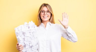 Güzel sarışın kız gülümsüyor ve arkadaş canlısı görünüyor, beş numarayı gösteriyor. kağıt toplar çöp konsepti