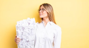 Profil görünümündeki güzel sarışın kız hayal mi kuruyor, hayal mi kuruyor yoksa hayal mi kuruyor? kağıt toplar çöp konsepti