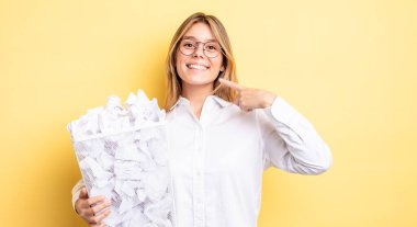 Güzel sarışın kız kendi gülüşünü göstererek kendine güvenerek gülümsüyor. kağıt toplar çöp konsepti