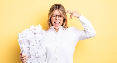 Güzel sarışın kız mutsuz ve stresli görünüyor, intihar jesti silah işareti yapıyor. kağıt toplar çöp konsepti