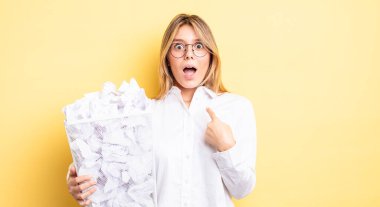 Şok olmuş ve ağzı açık, kendini işaret eden güzel sarışın bir kız. kağıt toplar çöp konsepti