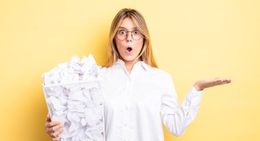 Güzel sarışın kız şaşırmış ve şok olmuş görünüyor. Çenesi düşmüş ve elinde bir nesne var. kağıt toplar çöp konsepti