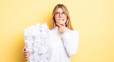 Güzel sarışın kız düşünüyor, kuşkulu ve şaşkın hissediyor. kağıt toplar çöp konsepti