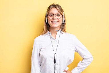 Güzel sarışın kız mutlu bir şekilde gülümsüyor, eli kalçasında ve kendinden emin. kulaklık konsepti