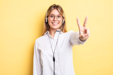 Güzel sarışın kız gülümsüyor ve mutlu görünüyor, zafer ya da barış işareti yapıyor. kulaklık konsepti