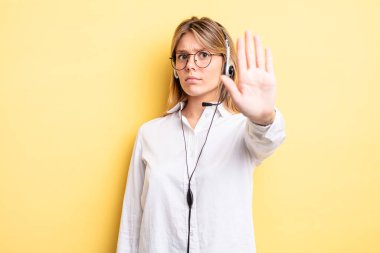 Güzel sarışın kız ciddi görünüyor. Avuç içini gösteriyor. Durma hareketi yapıyor. kulaklık konsepti