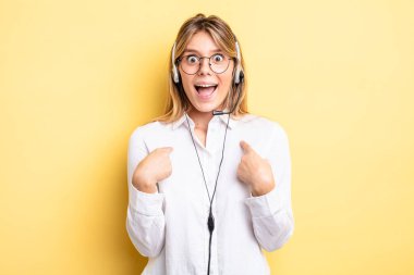 Güzel sarışın kız mutlu hissediyor ve heyecanla kendini işaret ediyor. kulaklık konsepti