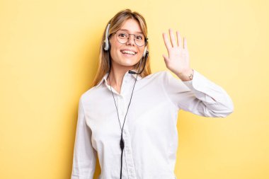 Güzel sarışın kız mutlu bir şekilde gülümsüyor, el sallıyor, hoş geldin diyor ve seni selamlıyor. kulaklık konsepti