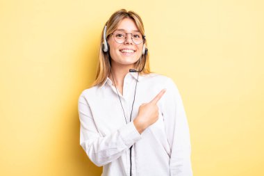 Güzel sarışın kız neşeyle gülümsüyor, mutlu hissediyor ve bir tarafı işaret ediyor. kulaklık konsepti