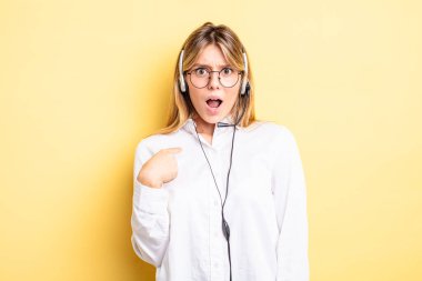 Şok olmuş ve ağzı açık, kendini işaret eden güzel sarışın bir kız. kulaklık konsepti