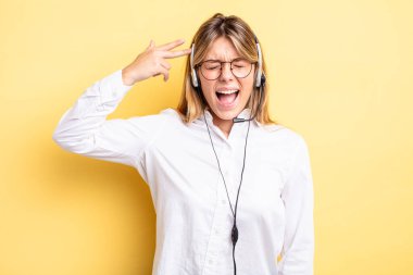 Güzel sarışın kız mutsuz ve stresli görünüyor, intihar jesti silah işareti yapıyor. kulaklık konsepti