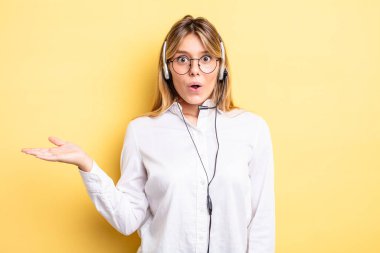 Güzel sarışın kız şaşırmış ve şok olmuş görünüyor. Çenesi düşmüş ve elinde bir nesne var. kulaklık konsepti