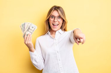 Güzel sarışın kız seni seçen kamerayı işaret ediyor. Dolar banknotları konsepti
