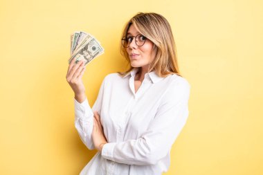 Güzel sarışın kız omuz silkiyor, kafası karışık ve kararsız. Dolar banknotları konsepti