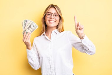 Güzel sarışın kız gülümsüyor ve arkadaş canlısı görünüyor. Bir numarayı gösteriyor. Dolar banknotları konsepti