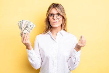 Güzel sarışın kız kapiş ya da para hareketi yapıyor, sana ödemeni söylüyor. Dolar banknotları konsepti