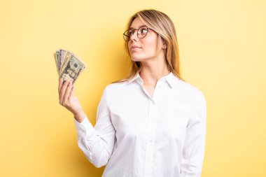 Profil görünümündeki güzel sarışın kız hayal mi kuruyor, hayal mi kuruyor yoksa hayal mi kuruyor? Dolar banknotları konsepti