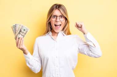 Güzel sarışın kız sinirli bir ifadeyle agresif bir şekilde bağırıyor. Dolar banknotları konsepti