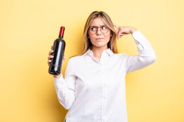 Güzel sarışın kız şaşkın ve kafası karışık, kaşınan bir kafa hissediyor. şarap şişesi konsepti