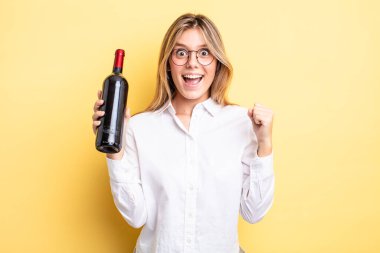 Güzel sarışın kız şokta, gülüyor ve başarıyı kutluyor. şarap şişesi konsepti
