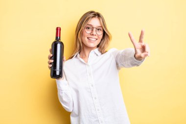 Güzel sarışın kız gülümsüyor ve mutlu görünüyor, zafer ya da barış işareti yapıyor. şarap şişesi konsepti