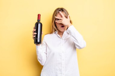 Güzel sarışın kız şok olmuş, korkmuş ya da korkmuş görünüyor. Yüzü elle kapatılmış. şarap şişesi konsepti