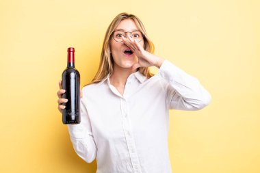 Güzel sarışın kız kendini mutlu hissediyor, elleri ağzının kenarında bağırıyor. şarap şişesi konsepti