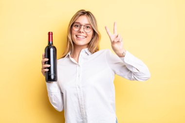 Güzel sarışın kız gülümsüyor ve arkadaş canlısı görünüyor. İki numarayı gösteriyor. şarap şişesi konsepti