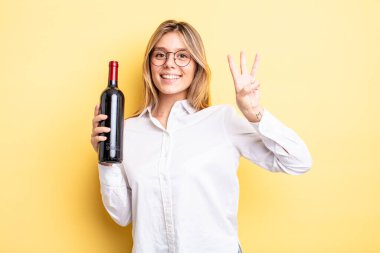 Güzel sarışın kız gülümsüyor ve arkadaş canlısı görünüyor, üç numarayı gösteriyor. şarap şişesi konsepti
