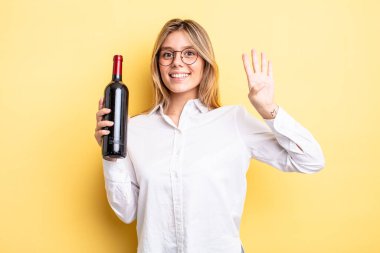 Güzel sarışın kız gülümsüyor ve arkadaş canlısı görünüyor, dört numarayı gösteriyor. şarap şişesi konsepti