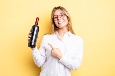 Güzel sarışın kız neşeyle gülümsüyor, mutlu hissediyor ve bir tarafı işaret ediyor. şarap şişesi konsepti
