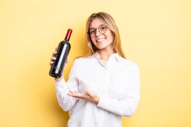 Güzel sarışın kız neşeyle gülümsüyor, mutlu hissediyor ve bir konsept gösteriyor. şarap şişesi konsepti