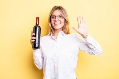 Güzel sarışın kız gülümsüyor ve arkadaş canlısı görünüyor, beş numarayı gösteriyor. şarap şişesi konsepti