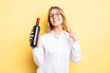 Güzel sarışın kız kendi gülüşünü göstererek kendine güvenerek gülümsüyor. şarap şişesi konsepti