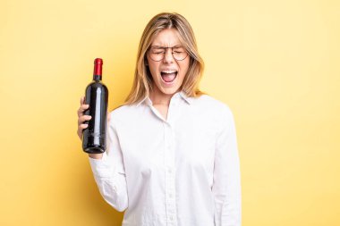 Güzel sarışın kız agresif bir şekilde bağırıyor, çok kızgın görünüyor. şarap şişesi konsepti