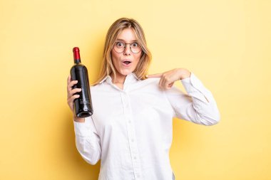 Şok olmuş ve ağzı açık, kendini işaret eden güzel sarışın bir kız. şarap şişesi konsepti