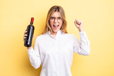 Güzel sarışın kız sinirli bir ifadeyle agresif bir şekilde bağırıyor. şarap şişesi konsepti