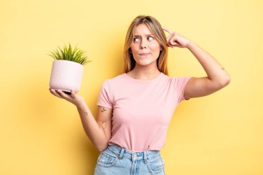 Güzel sarışın kız mutlu bir şekilde gülümsüyor ve hayal kuruyor ya da şüphe ediyor. ev bitkisi kavramı