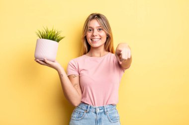 Güzel sarışın kız seni seçen kamerayı işaret ediyor. ev bitkisi kavramı