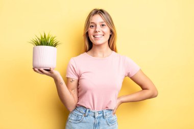 Güzel sarışın kız mutlu bir şekilde gülümsüyor, eli kalçasında ve kendinden emin. ev bitkisi kavramı