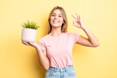 Güzel sarışın kız kendini mutlu hissediyor, iyi bir jestle onaylıyor. ev bitkisi kavramı