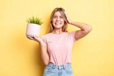 Güzel sarışın kız stresli, endişeli ya da korkmuş, elleri başının üstünde. ev bitkisi kavramı