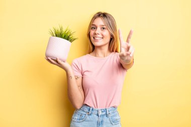 Güzel sarışın kız gülümsüyor ve mutlu görünüyor, zafer ya da barış işareti yapıyor. ev bitkisi kavramı