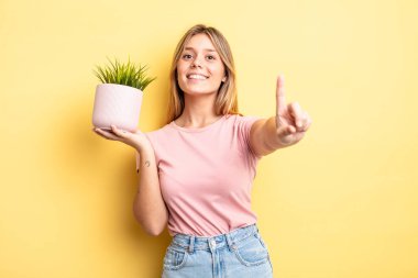 Güzel sarışın kız gururla gülümsüyor ve kendinden emin bir numara oluyor. ev bitkisi kavramı