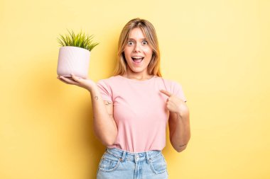 Güzel sarışın kız mutlu hissediyor ve heyecanla kendini işaret ediyor. ev bitkisi kavramı