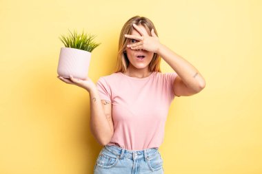 Güzel sarışın kız şok olmuş, korkmuş ya da korkmuş görünüyor. Yüzü elle kapatılmış. ev bitkisi kavramı
