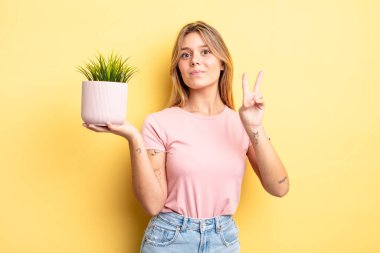 Güzel sarışın kız gülümsüyor ve arkadaş canlısı görünüyor. İki numarayı gösteriyor. ev bitkisi kavramı